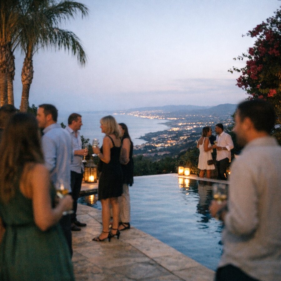 Invitados con copas junto a la piscina infinita de una villa sobre Marbella al anochecer